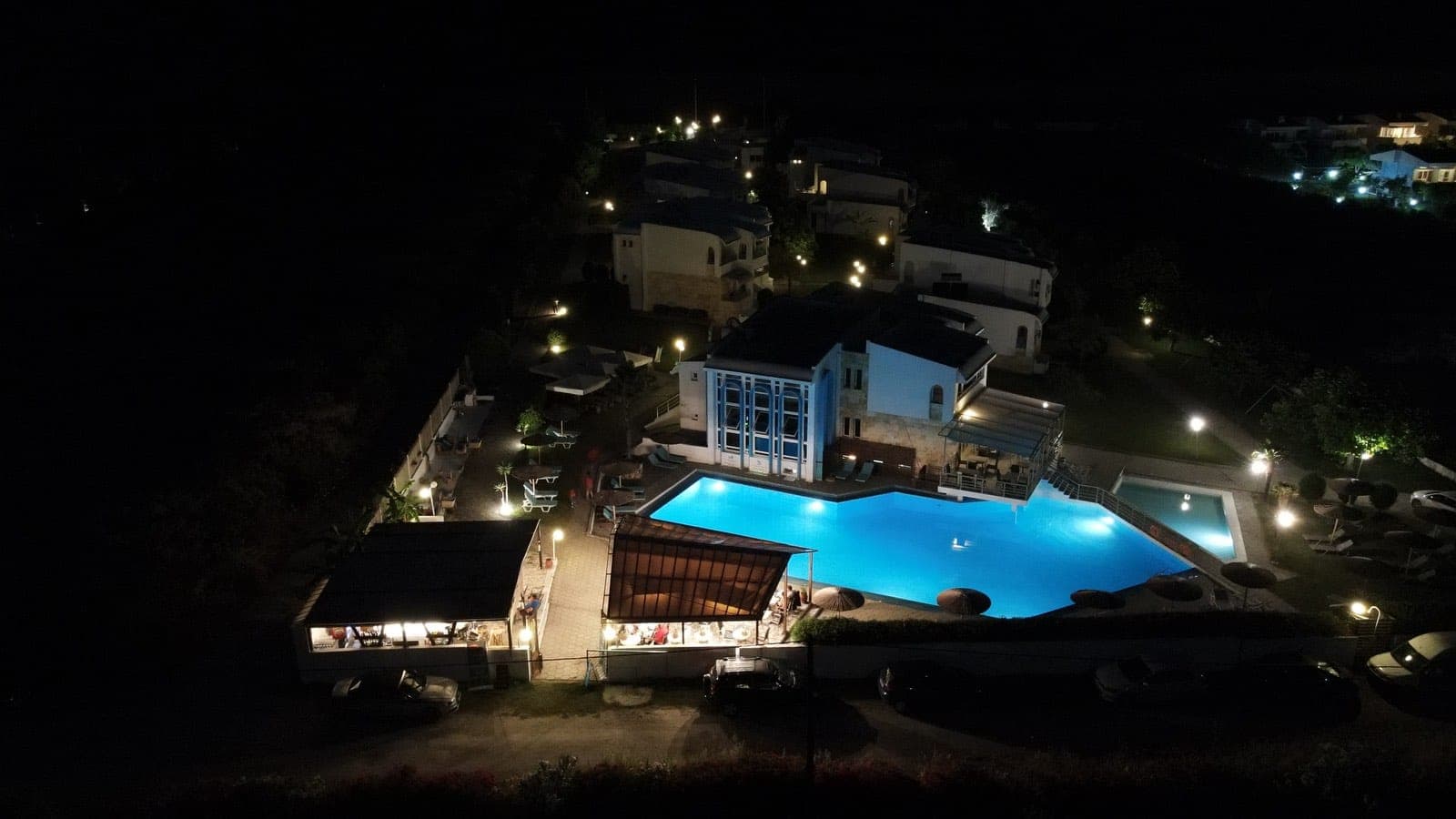 Elegant nighttime beachfront resort in Halkidiki with glowing infinity-style pools, atmospheric lighting, and relaxing Mediterranean summer ambiance.